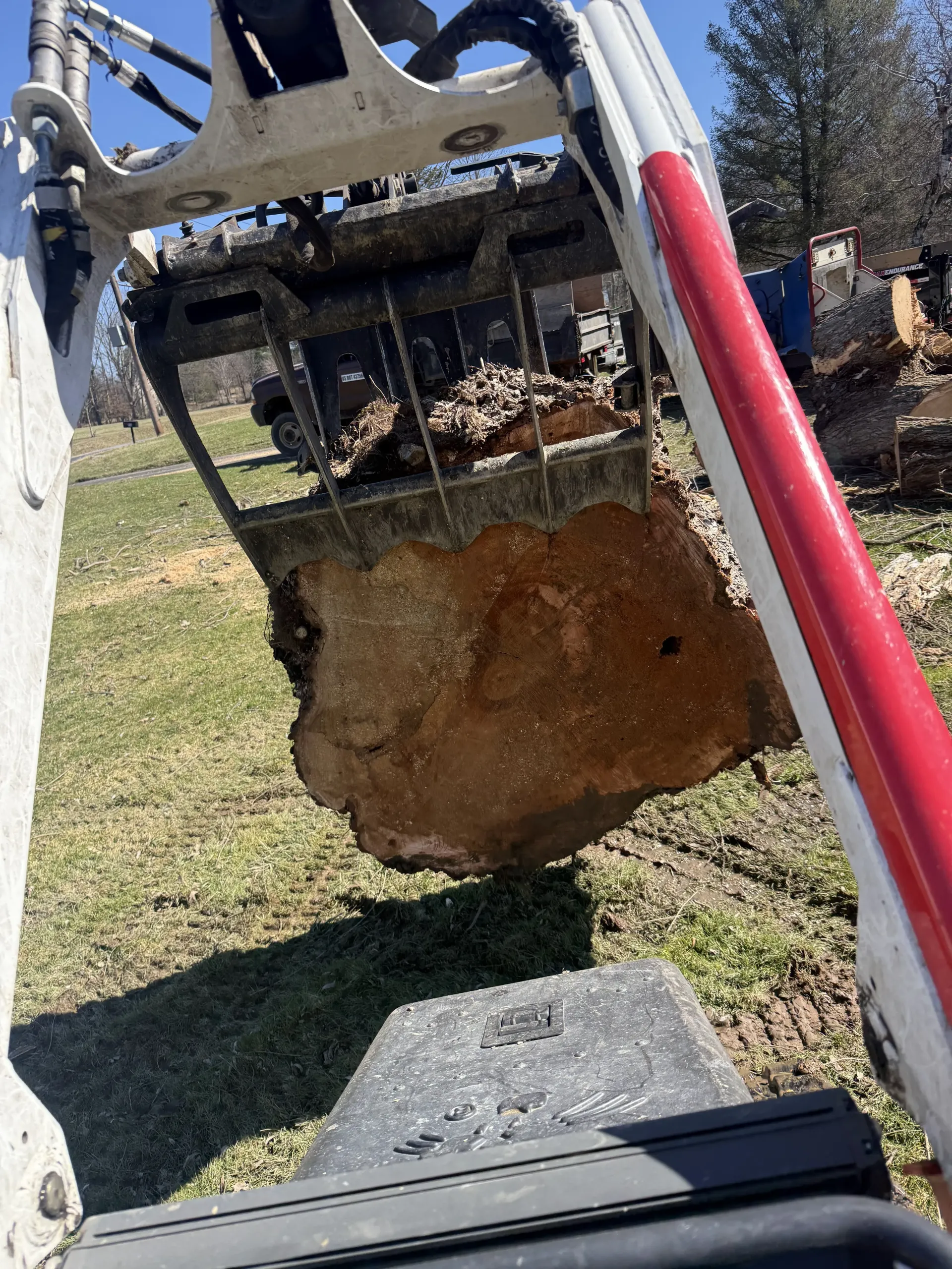 Excavator bucket lifting a large dirt-covered rock or root near a grassy hillside.