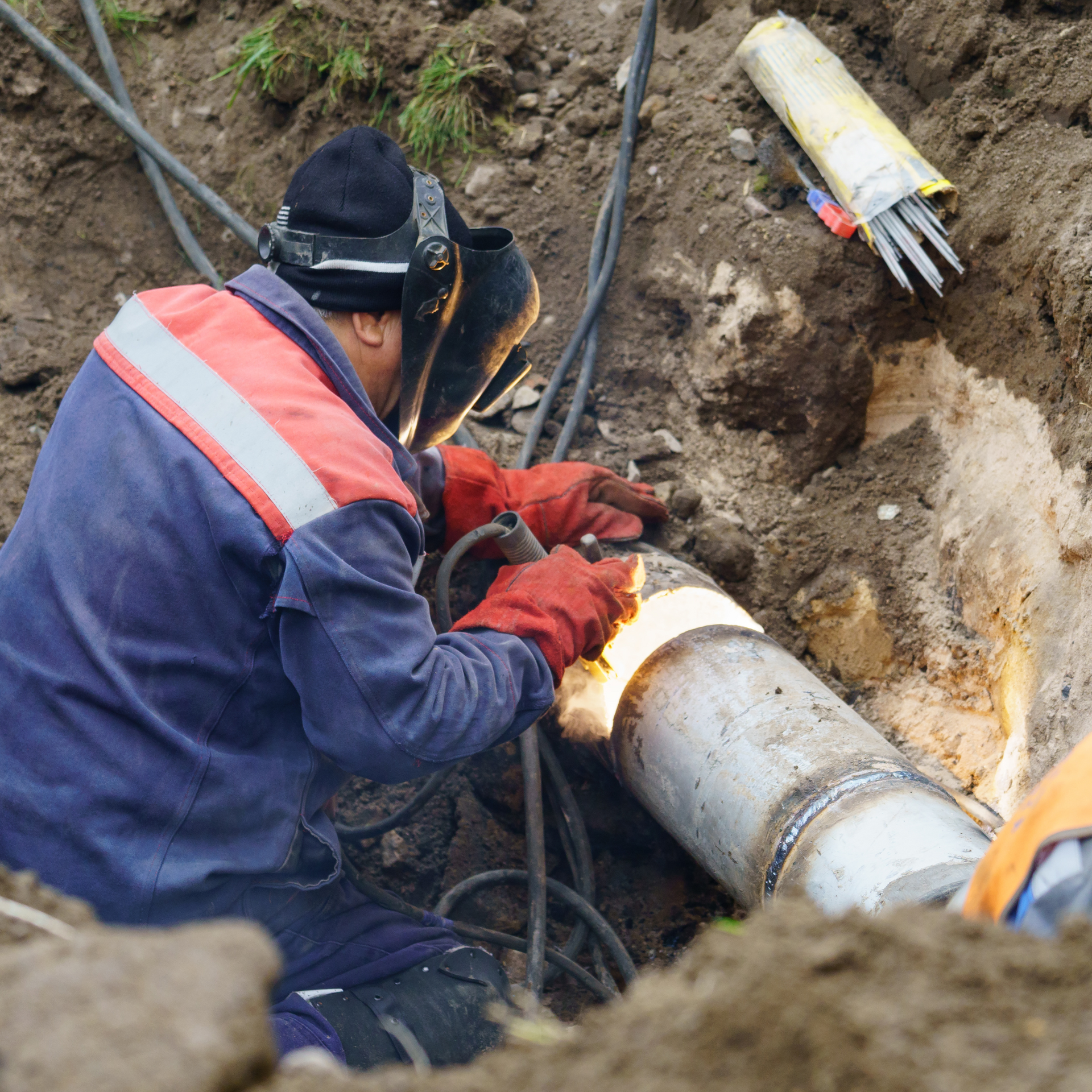 A man is welding a pipe in the dirt