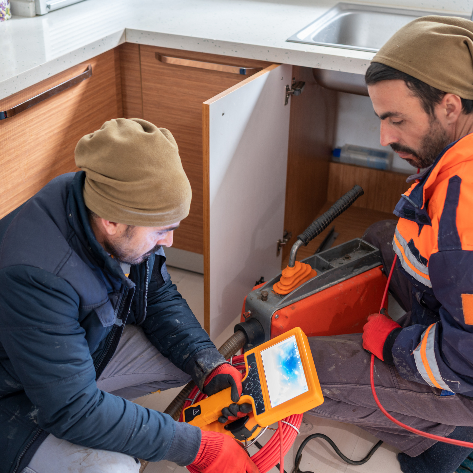 Two men are working on a drain in a kitchen.