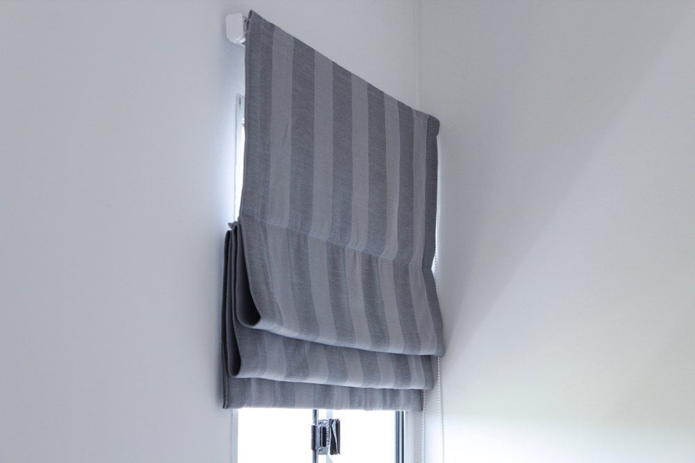Gray Striped Roman Shade Partially Covering a Small Window on a White Wall — Glenn Koek - Shutters - Curtains - Blinds in West Wollongong, NSW