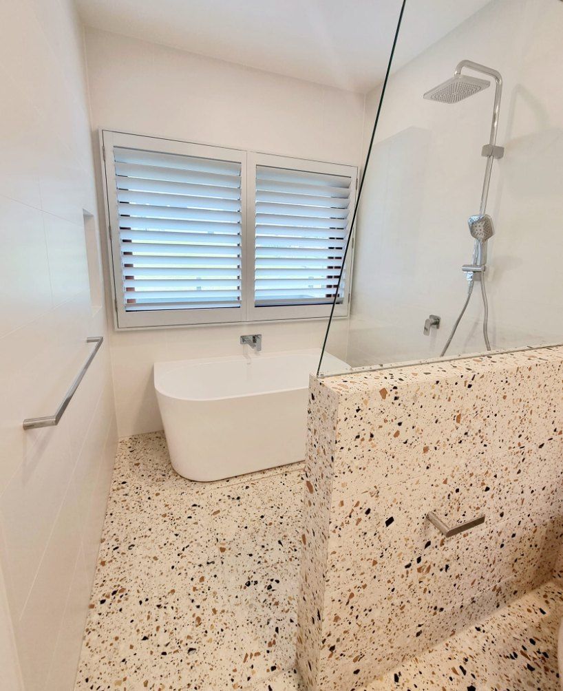 Bathroom with a white tub, terrazzo floor, and a shower with glass doors. — Glenn Koek - Shutters - Curtains - Blinds in Illawarra, NSW