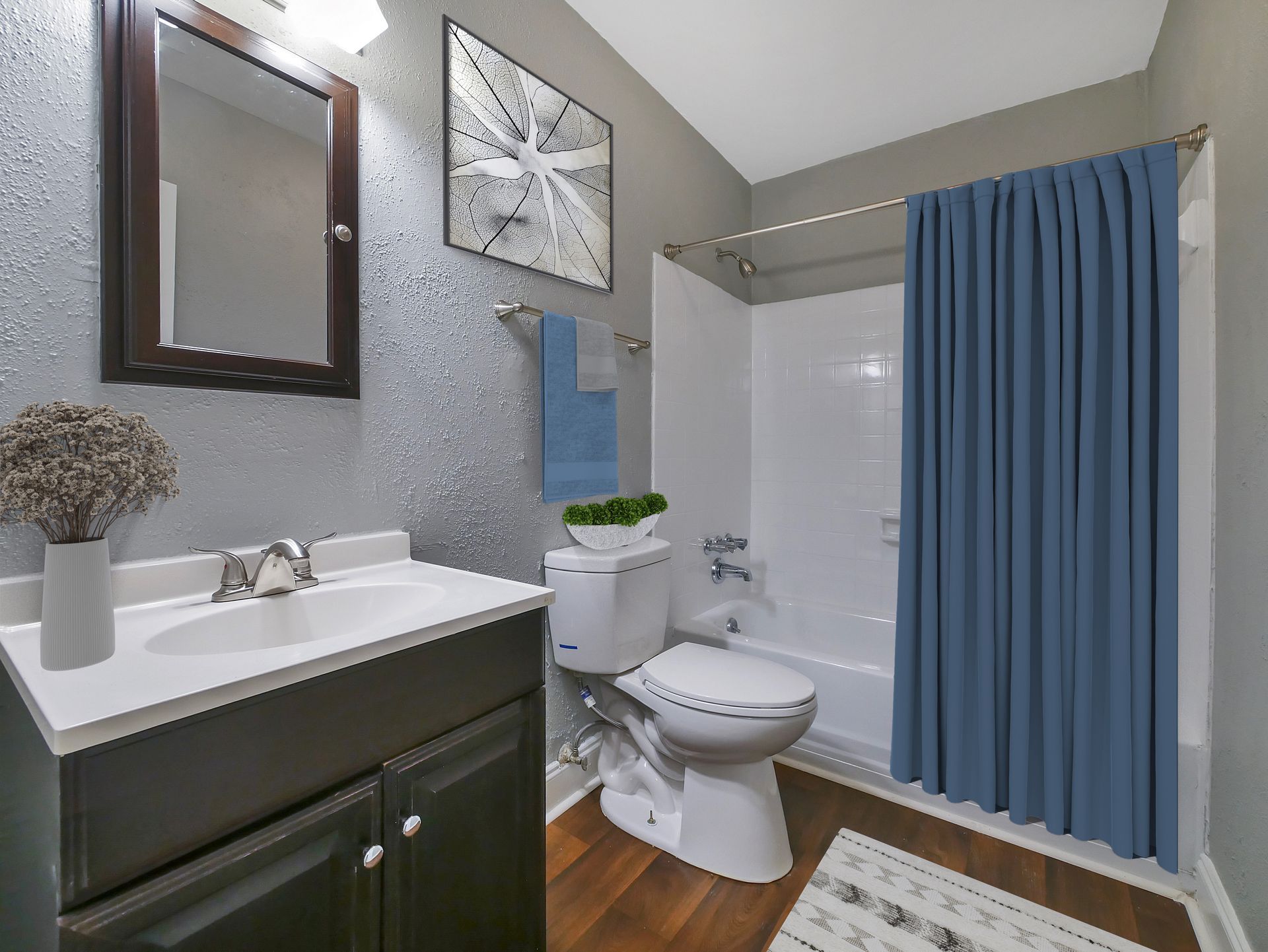 A modern bathroom with a dark wood vanity, white sink, textured grey wall, and a blue shower curtain over a bathtub.