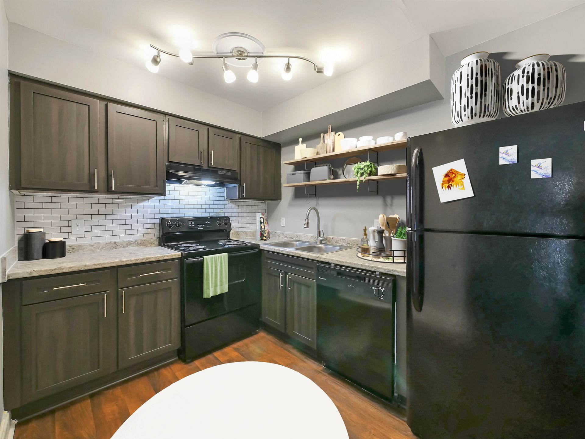 A kitchen with dark wood cabinets, black appliances, light stone countertops, and open shelving on a gray wall.