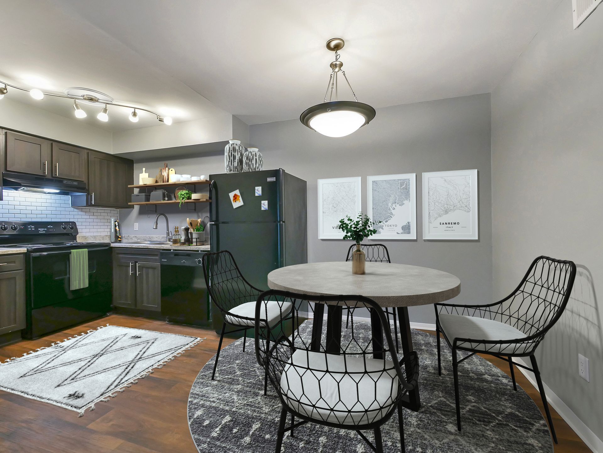 Dining area with a round stone table, four wire-frame chairs on a round rug, and a modern kitchen with dark cabinets.