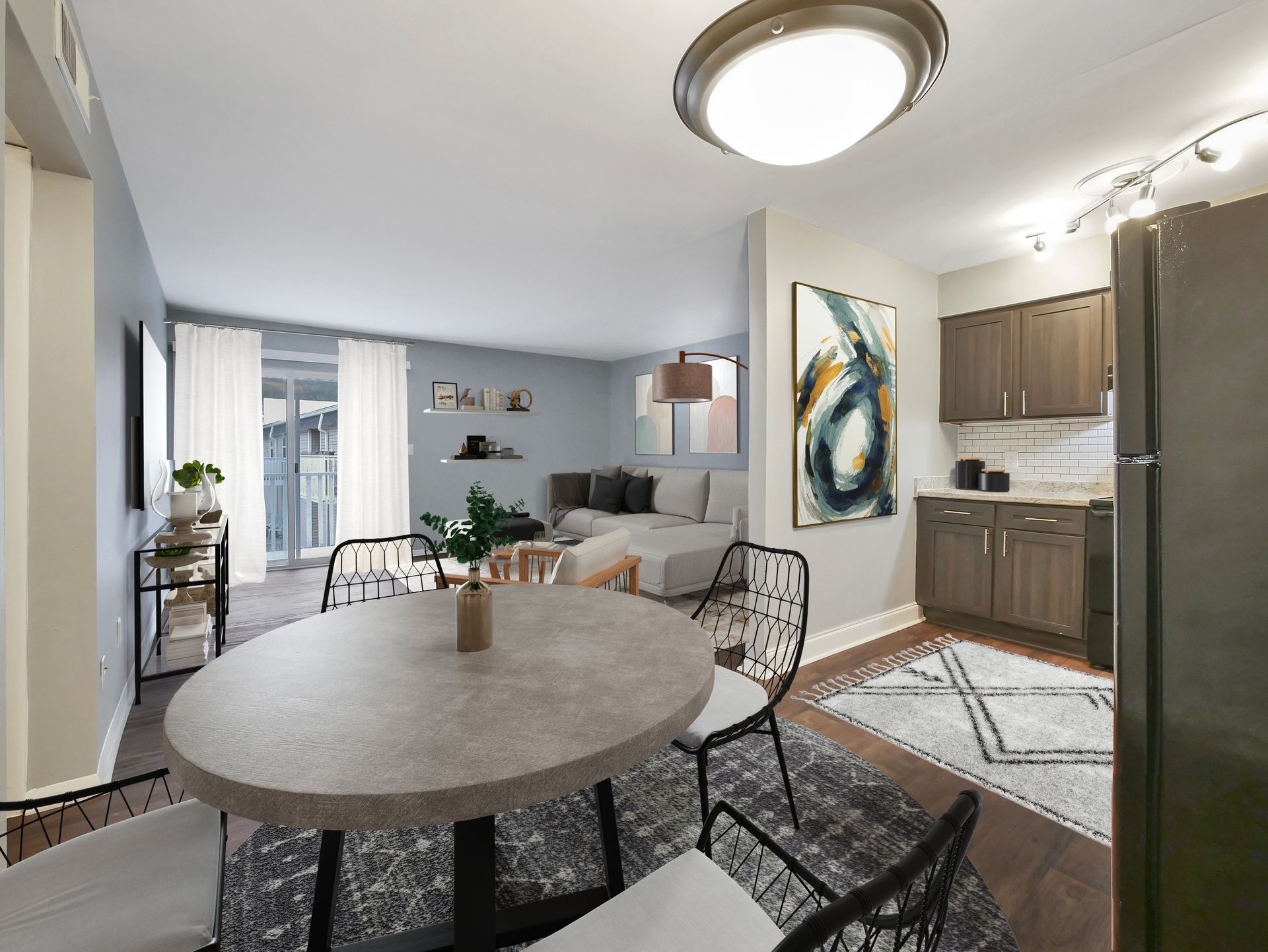 A dining area with a round stone table and chairs, leading into a living room and a kitchen with wooden cabinets.