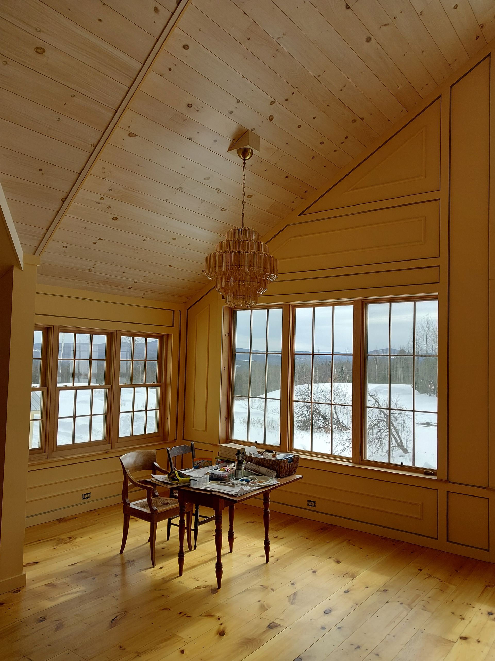 Sunlit wooden dining room with large windows, snow outside, and a table set for tea