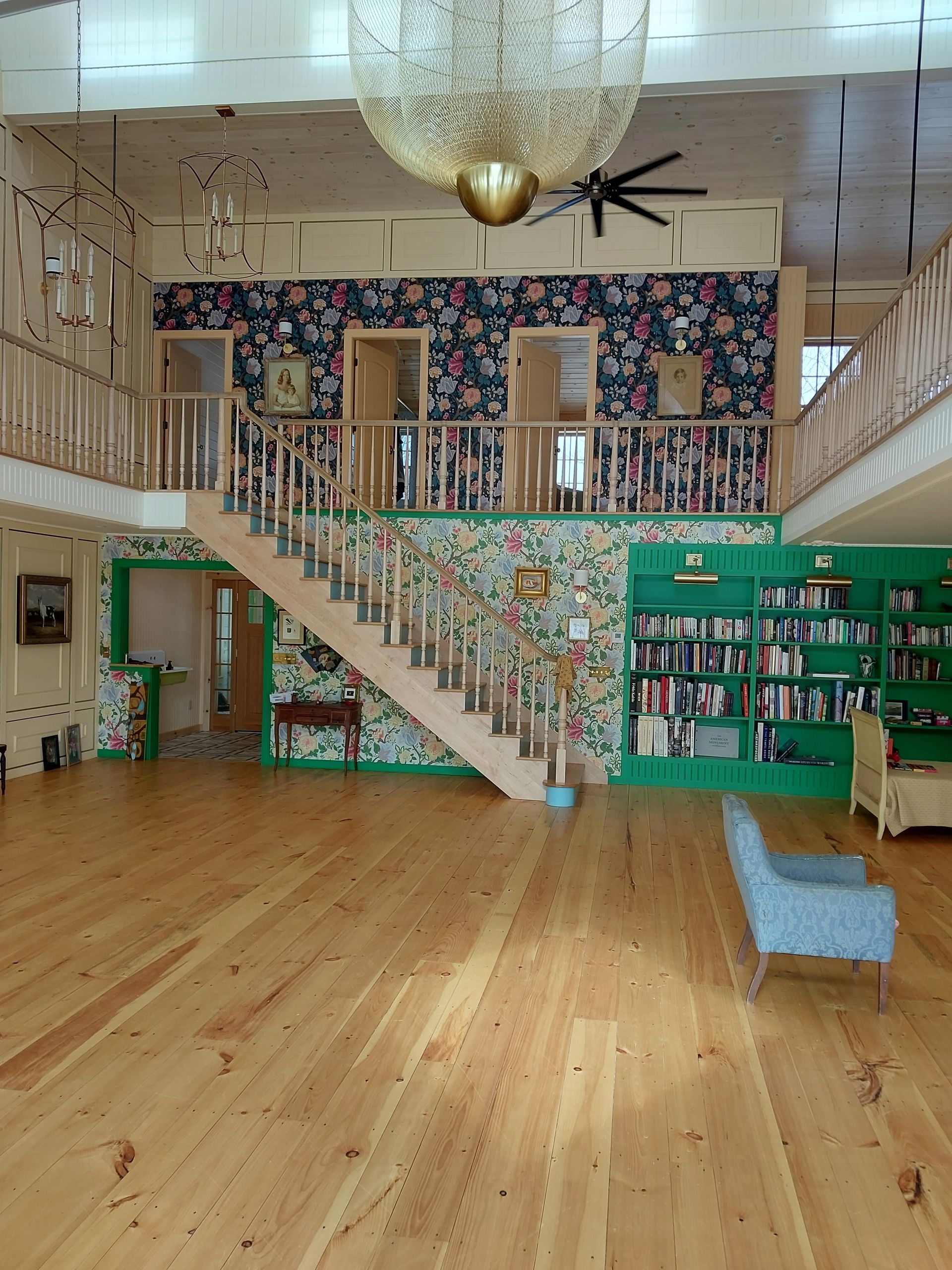 Bright library interior with staircase, bookshelves, and a blue chair on a wooden floor