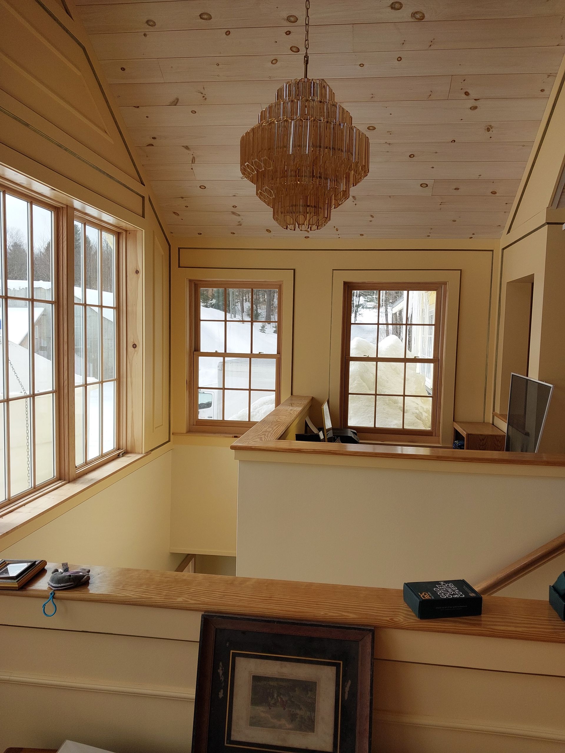 Cozy sunroom with wood-paneled walls, windows, a hanging light, and a countertop with framed art.
