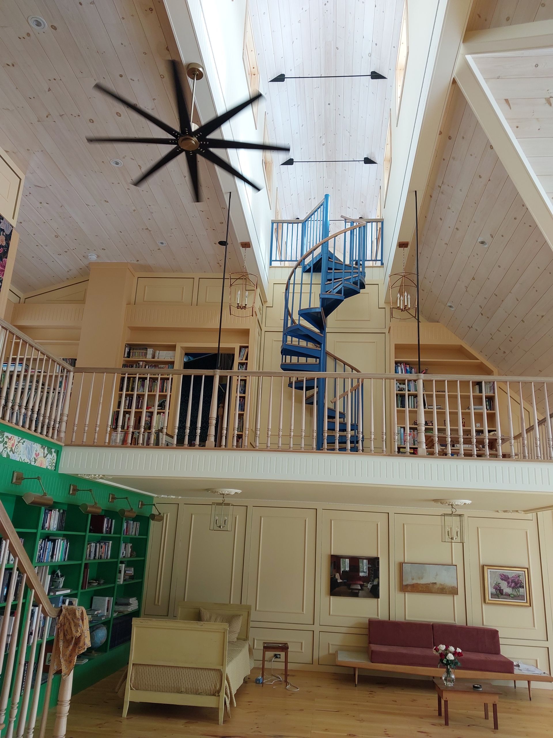Spacious lodge atrium with tall ceiling, large fan, blue spiral staircase, and seating area below