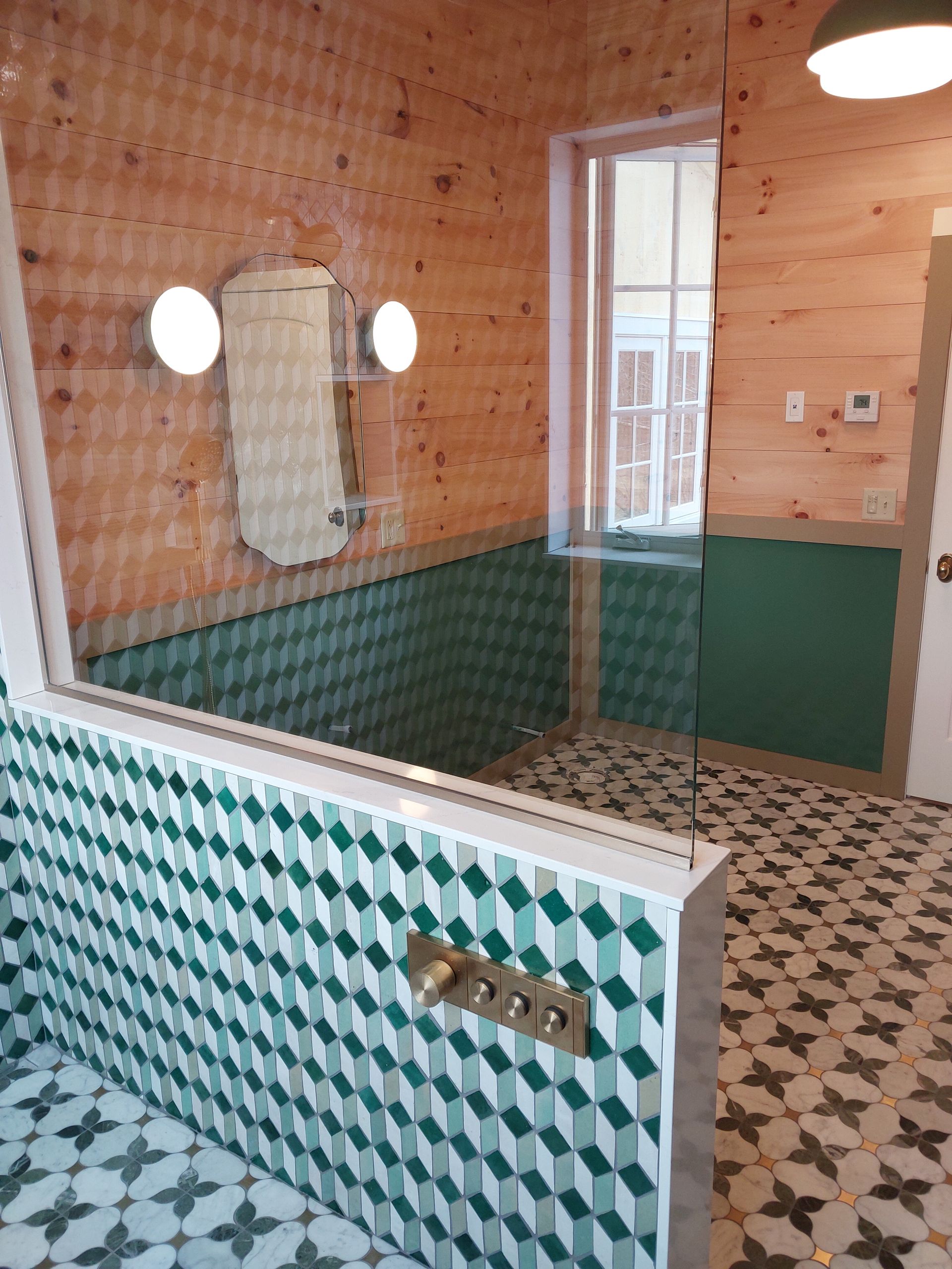 Sauna with wooden walls, patterned tile floor, glass-walled shower, and green tiled bench area