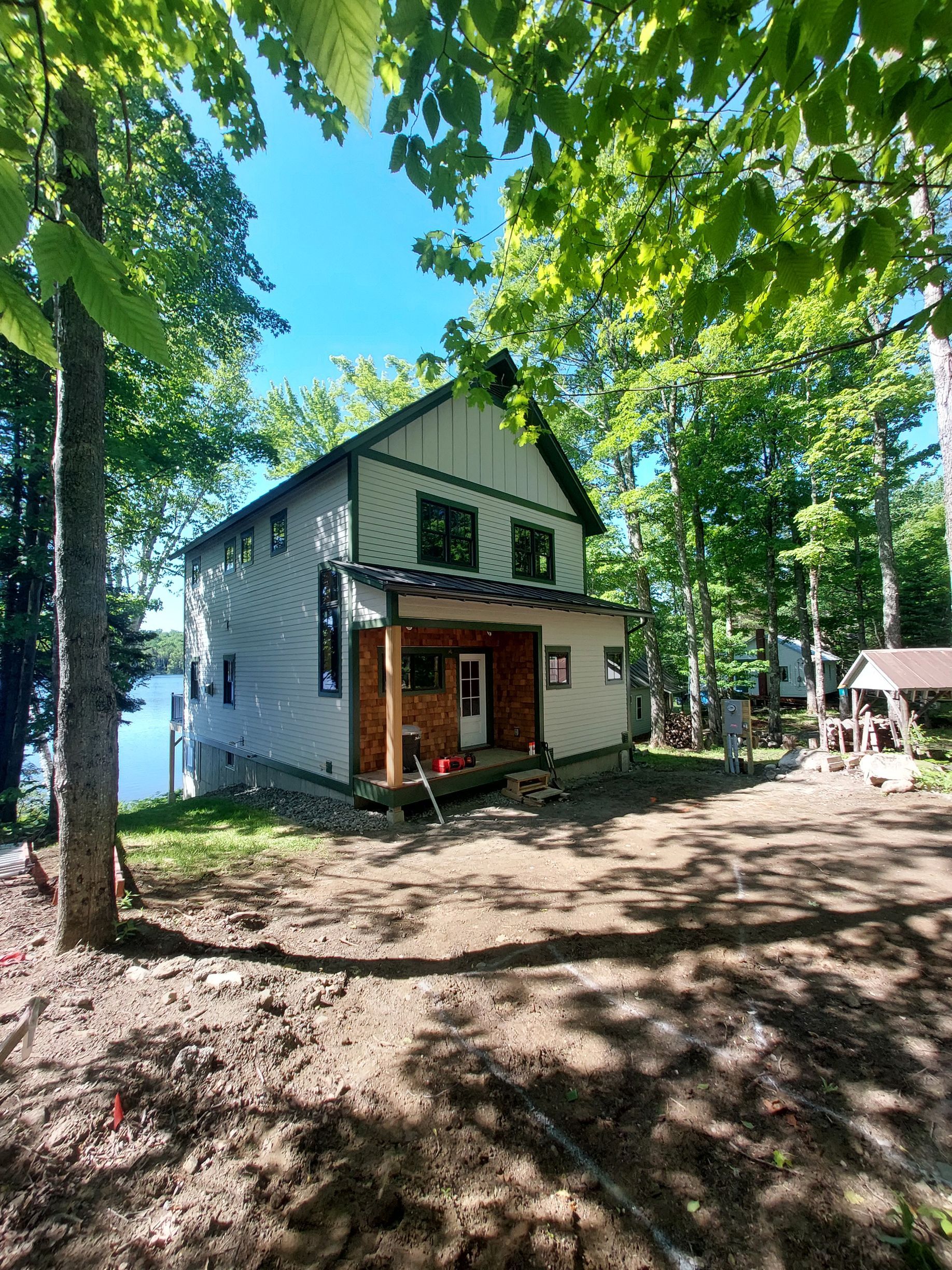 Two-story house with porch in a wooded yard, sunlight filtering through trees