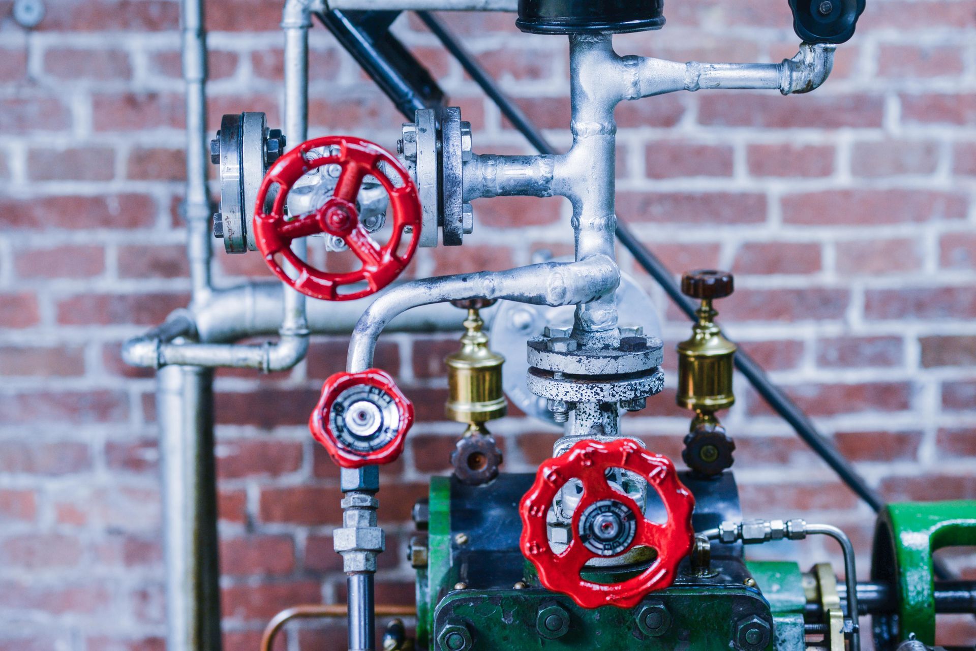 Industrial pipes with red valve wheels against a brick wall.