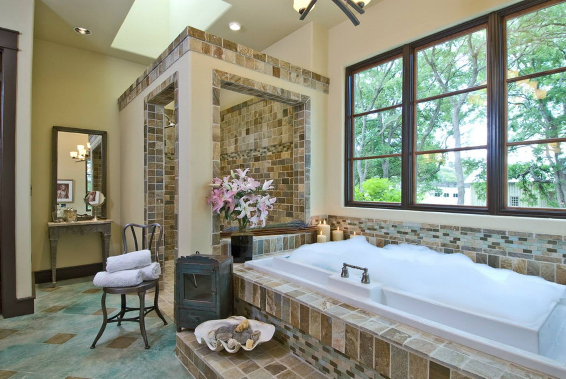Spa-style bathroom with tiled soaking tub, glass shower, vanity, and large windows overlooking greenery