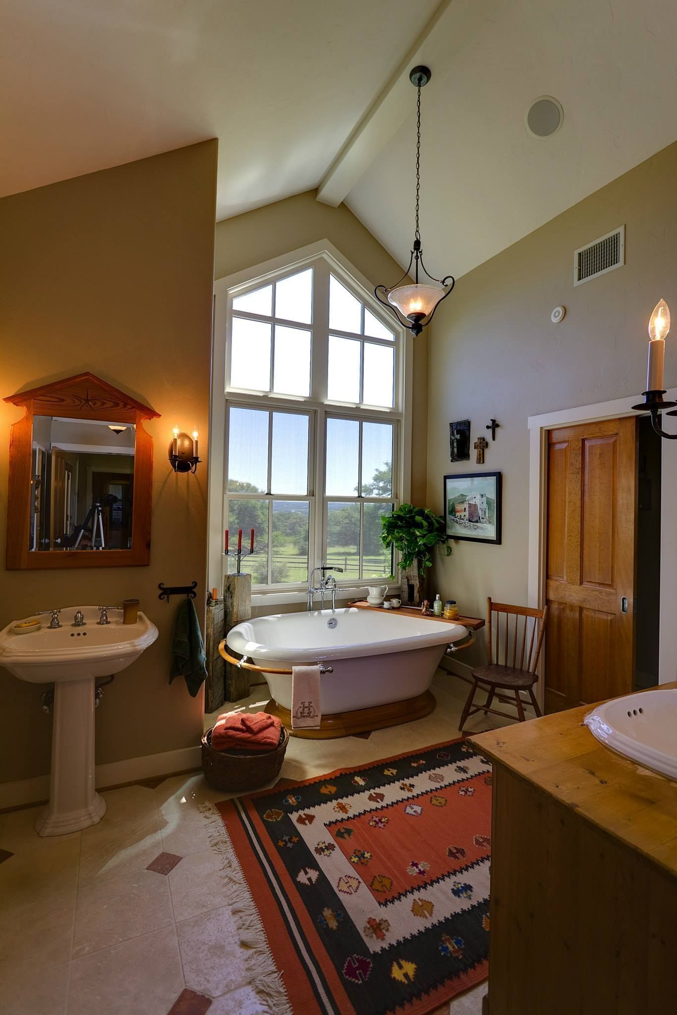 Elegant bathroom with a large window, clawfoot tub, pedestal sink, and warm earth-toned decor.