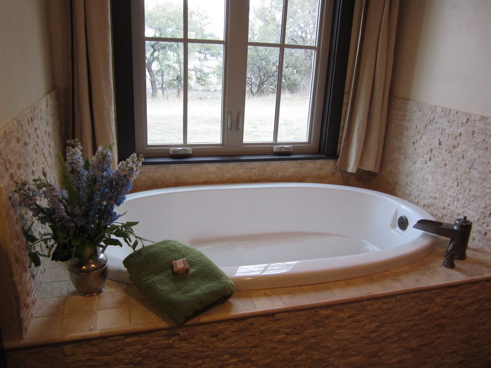 Bathroom with a white soaking tub by a window, granite ledge, green towel, and flowers on the left