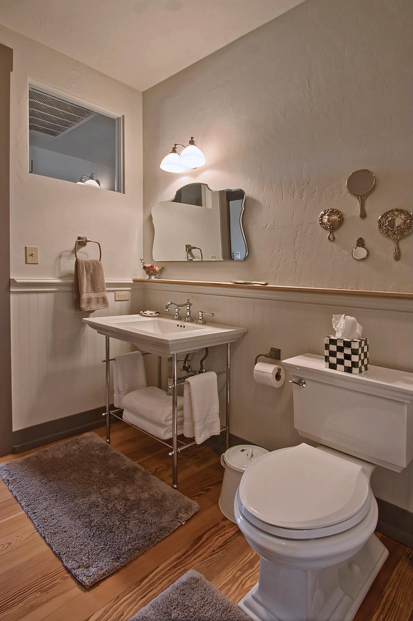 Small bathroom with white vanity, toilet, wall mirror, and decorative gold accents on beige walls.