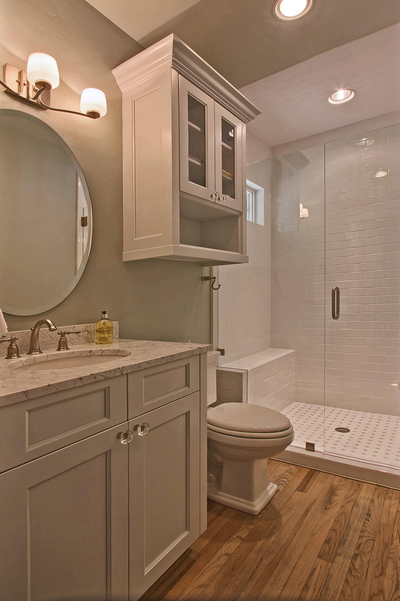 Modern bathroom with gray vanity, round mirror, toilet, and glass shower with white tile.