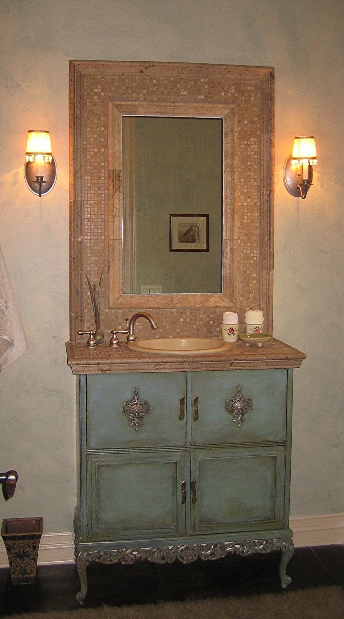 Vintage vanity with ornate mirror, aqua cabinet, and wall sconces in a softly lit room