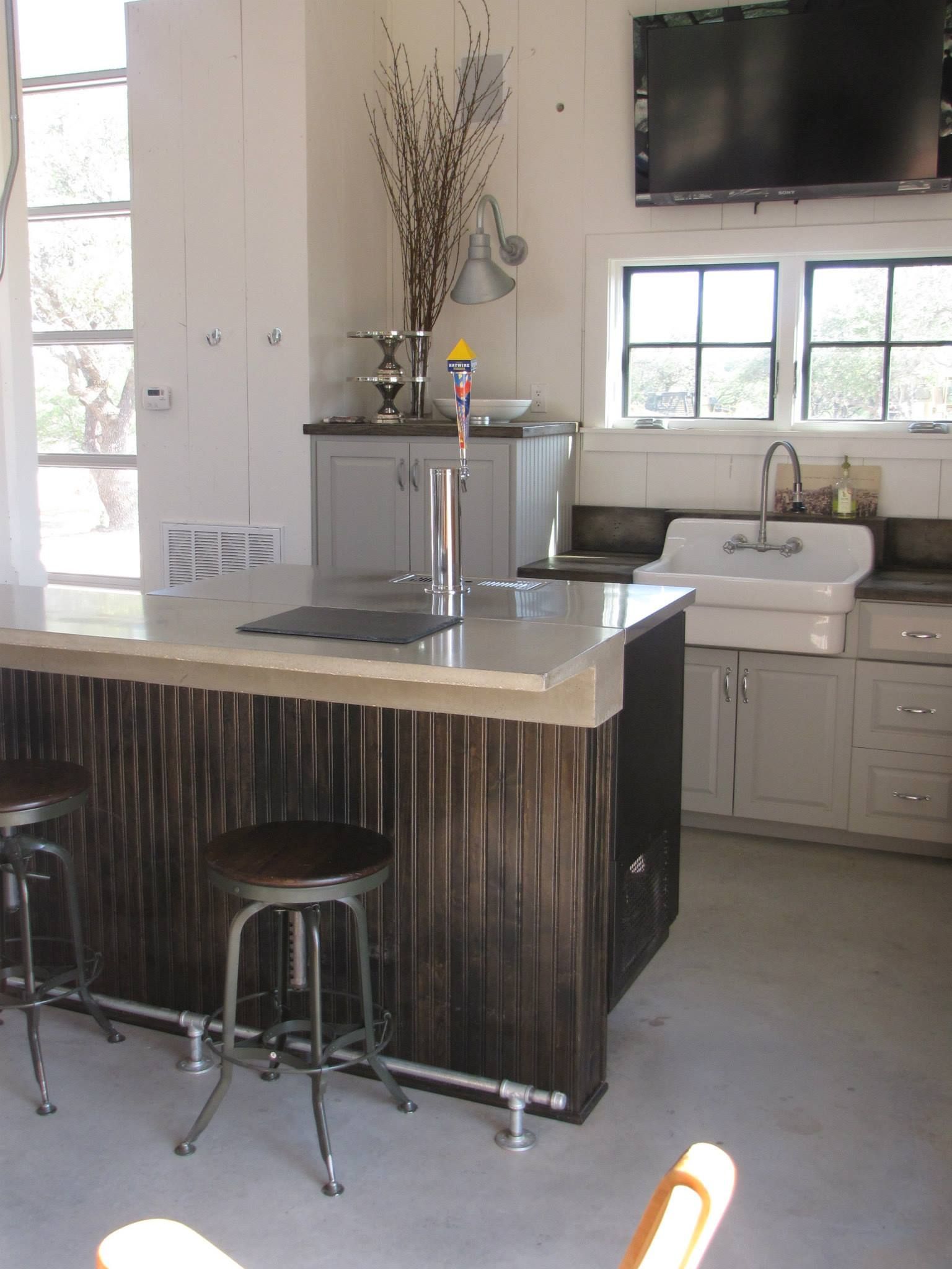 Modern kitchen with island, bar stools, sink, and wall-mounted TV above the counter.