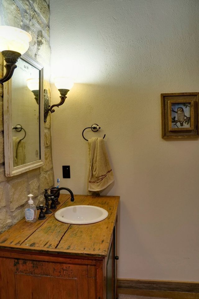 Small bathroom vanity with wooden counter, sink, mirror, and wall sconces beside a towel rack.