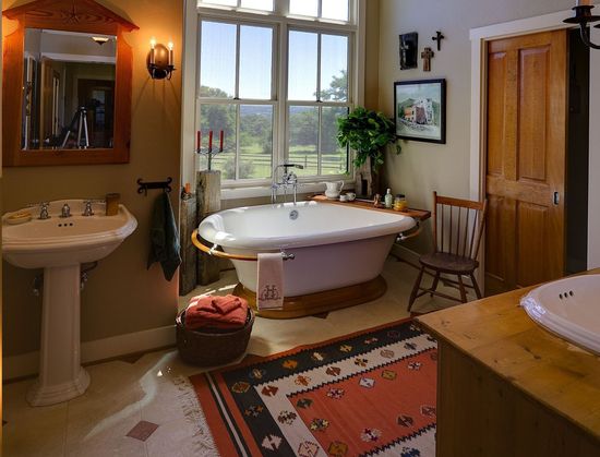 Bright bathroom with clawfoot tub, sink, wooden door, window view, and patterned rug.
