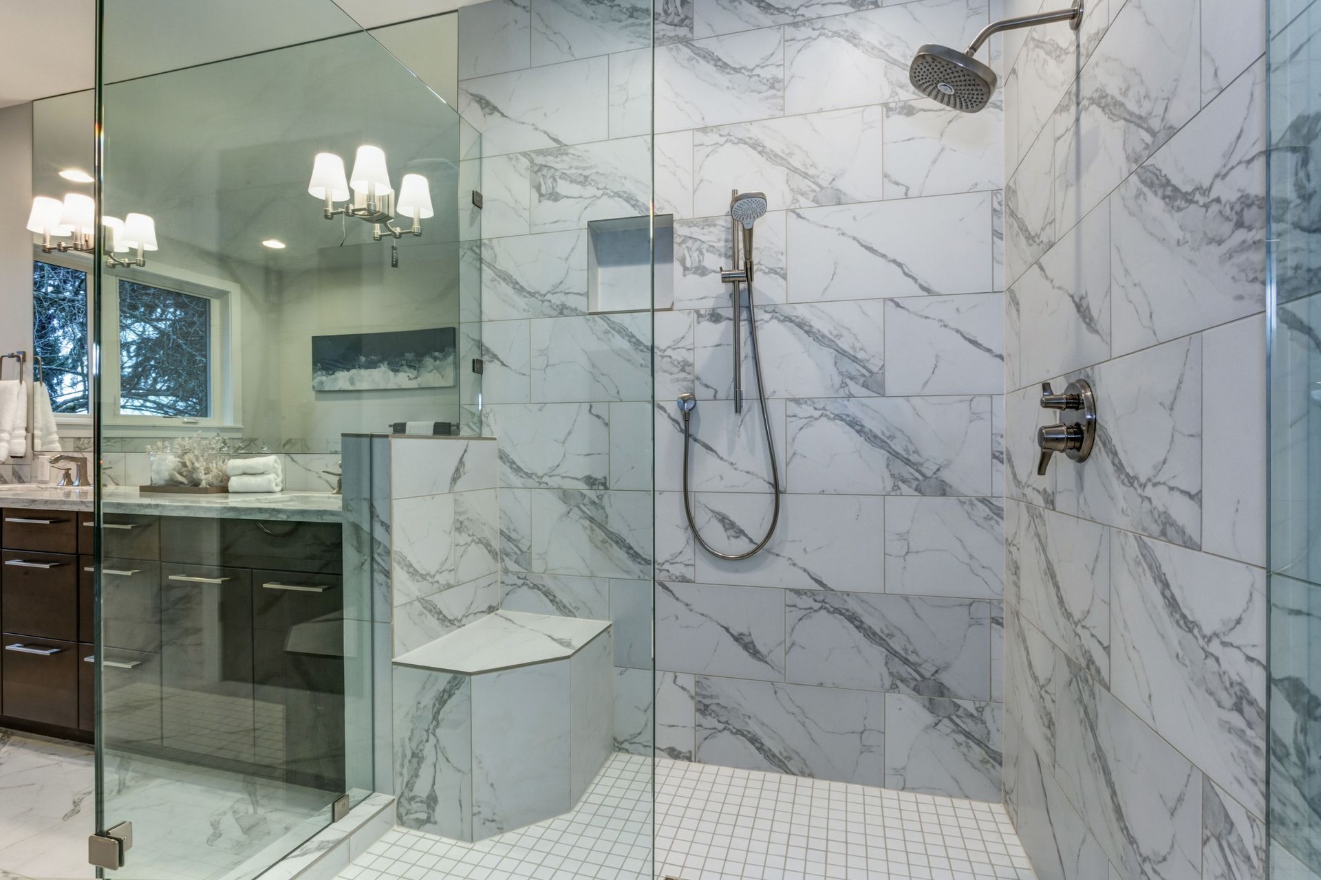 Modern bathroom with marble shower, glass enclosure, and vanity visible through the open door