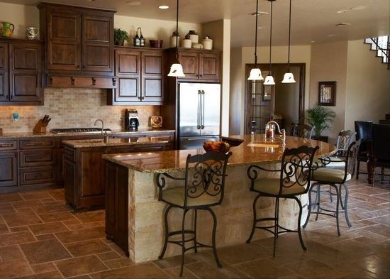 Warm kitchen with wood cabinets, stone island, pendant lights, and metal barstools on a tiled floor