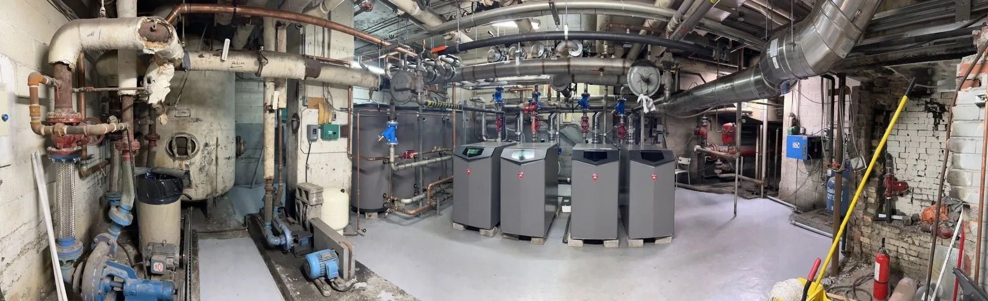 Sous-sol industriel avec de gros tuyaux, conduits, réservoirs et unités d'équipement gris dans une salle des machines