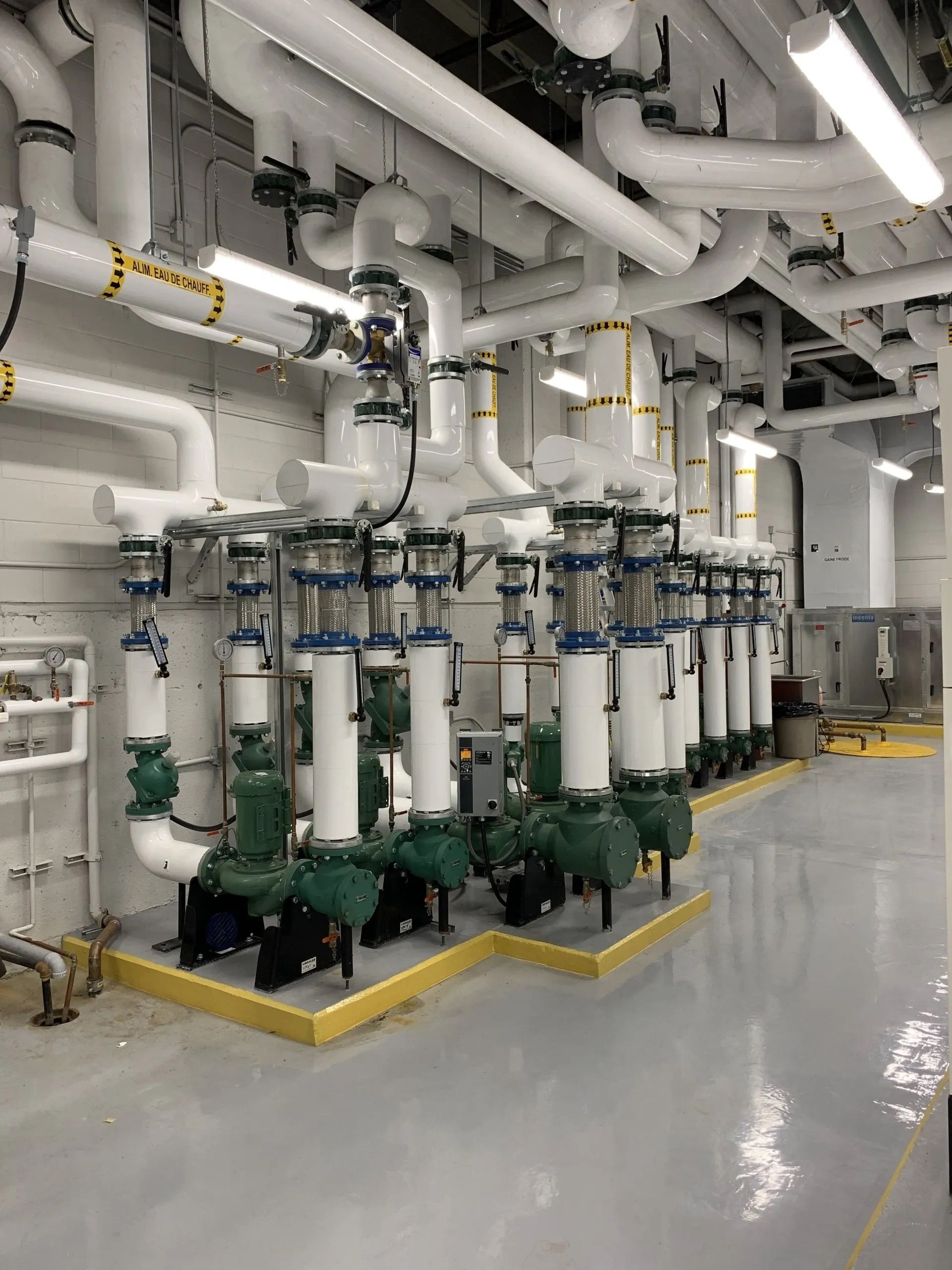 Industrial piping and filtration equipment in a clean mechanical room with white pipes and green bases