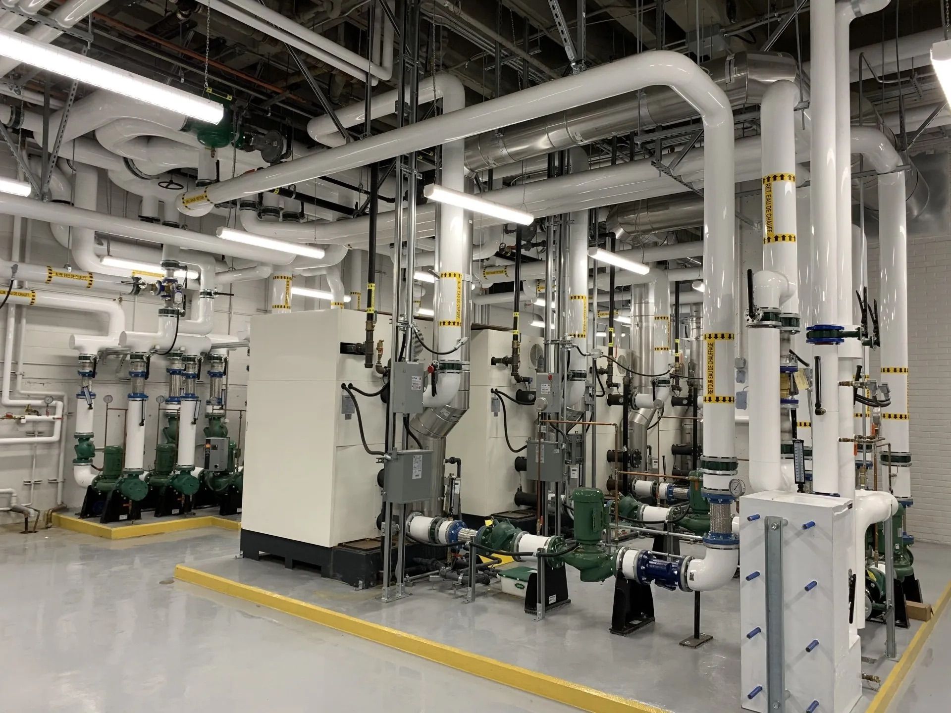 Industrial mechanical room with large white pipes, valves, and pumps on a clean concrete floor