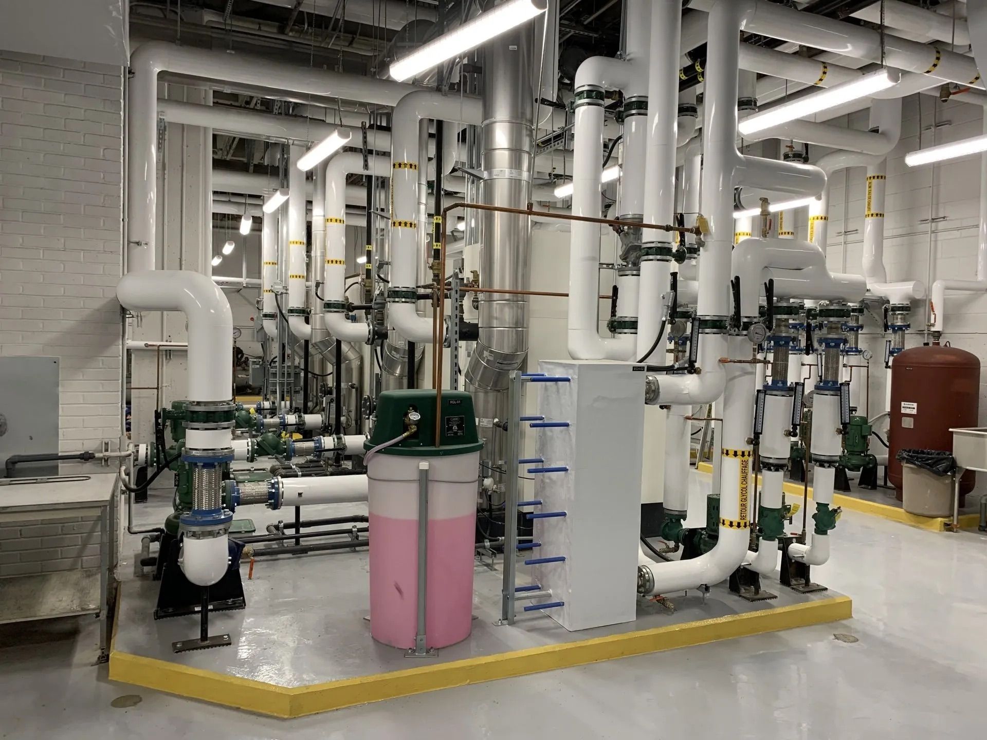 Industrial water treatment room with pipes, pumps, and white equipment on a concrete floor