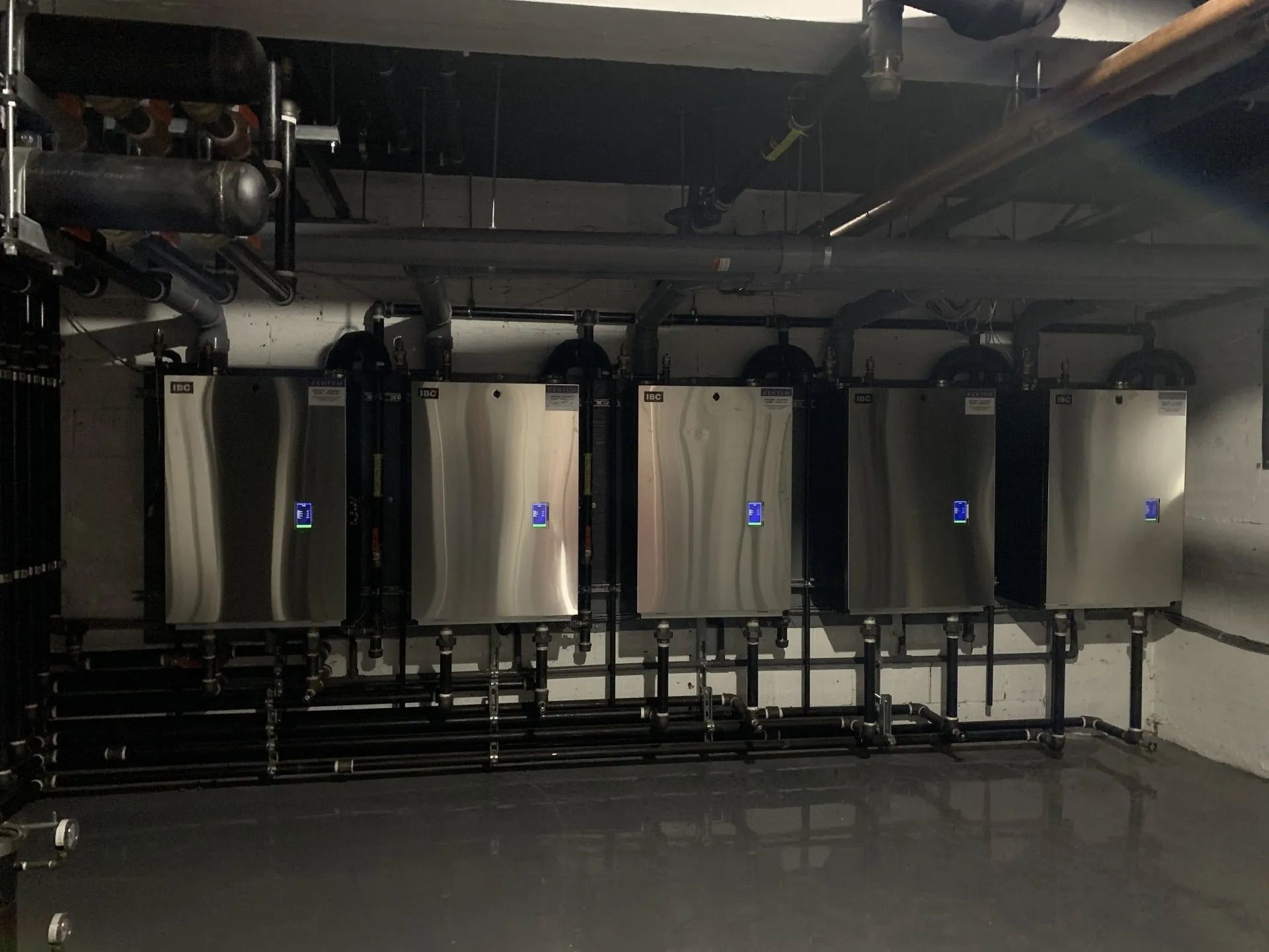 Rangée de grands réservoirs métalliques muraux dans un local technique industriel avec tuyauterie apparente et sol sombre