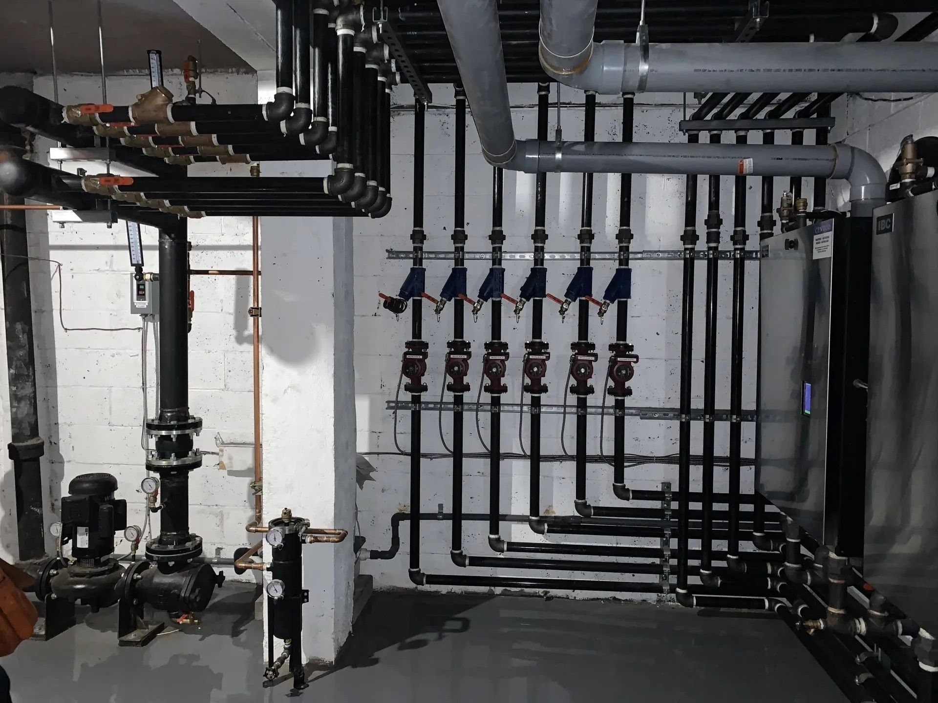 Sous-sol industriel avec tuyaux noirs apparents, vannes et canalisations blanches le long du mur