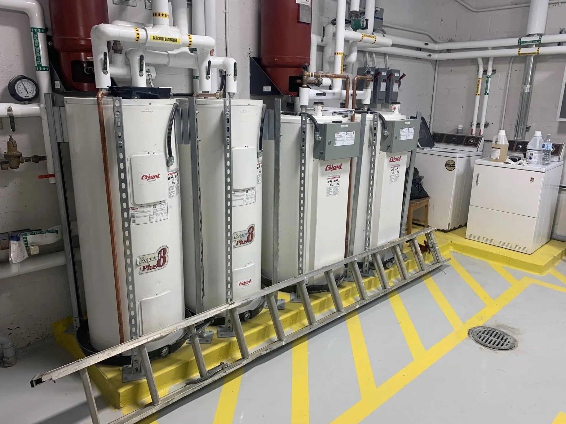 Industrial equipment with white tanks and pipes in a utility room, marked by yellow floor lines.