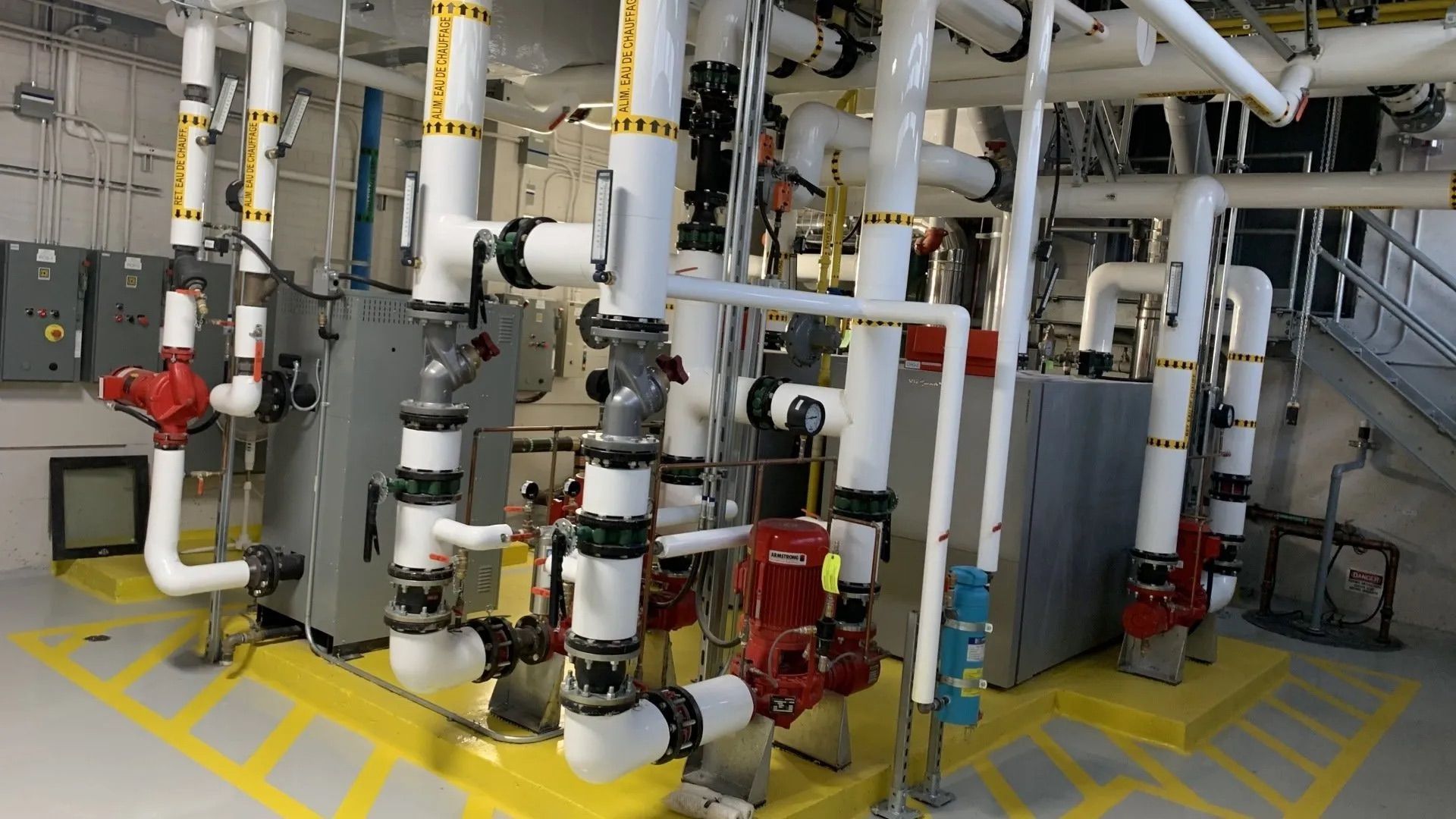 Industrial piping and valves in a mechanical room with yellow safety markings on the floor
