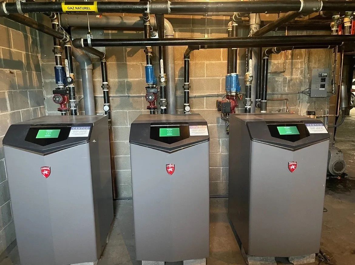 Three gray boilers with green display screens in a basement mechanical room