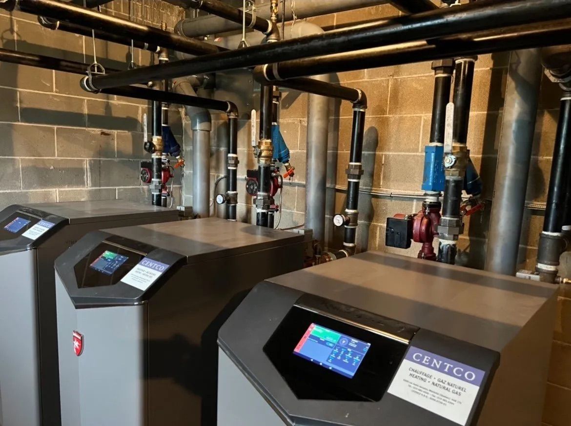 Basement boiler room with two large black HVAC units and exposed pipes against cinderblock walls