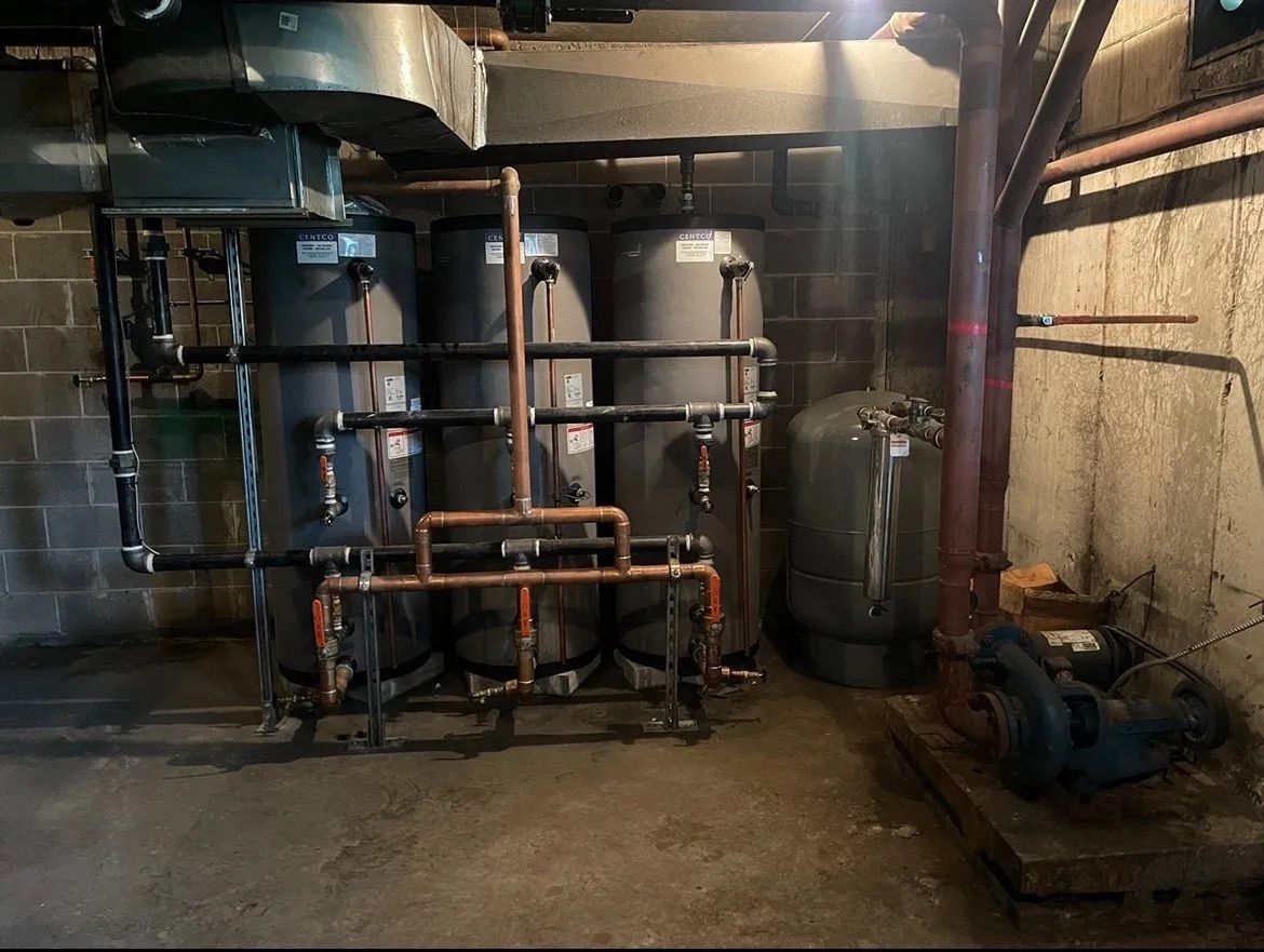 Sous-sol industriel avec de grandes cuves métalliques, des tuyaux et des pompes dans une buanderie sombre.