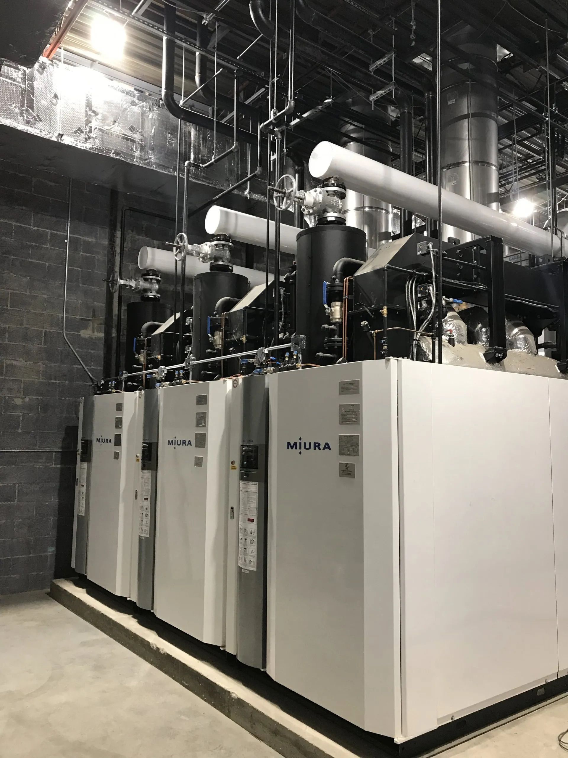 Rows of white industrial cooling units with pipes and machinery in a factory room