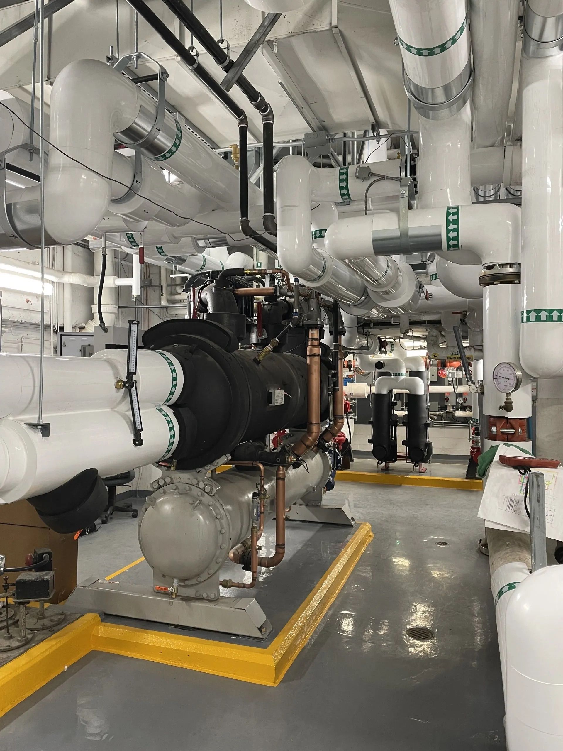 Industrial engine room with large white pipes, a black machine, and yellow floor safety markings