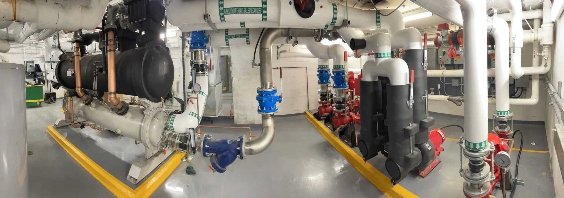 Industrial mechanical room with pipes, valves, pumps, and insulated equipment on a concrete floor