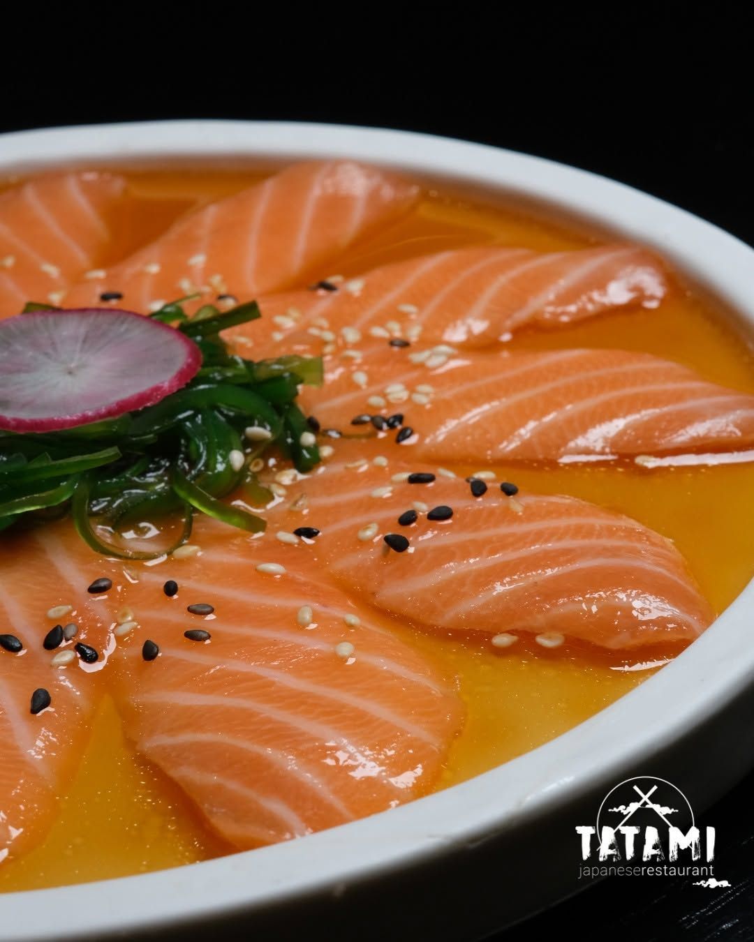 Sashimi di salmone disposto in una ciotola bianca con salsa all’arancia, alghe, ravanello e semi di sesamo nero