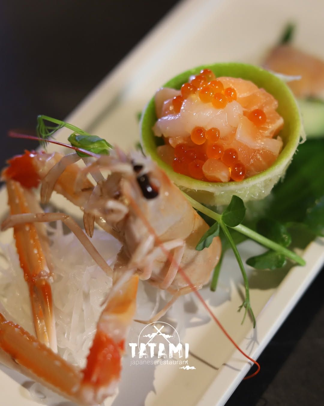 Assortimento di sushi impiattato con nigiri di gambero, uova di pesce arancioni e guarnizione verde su un piatto bianco