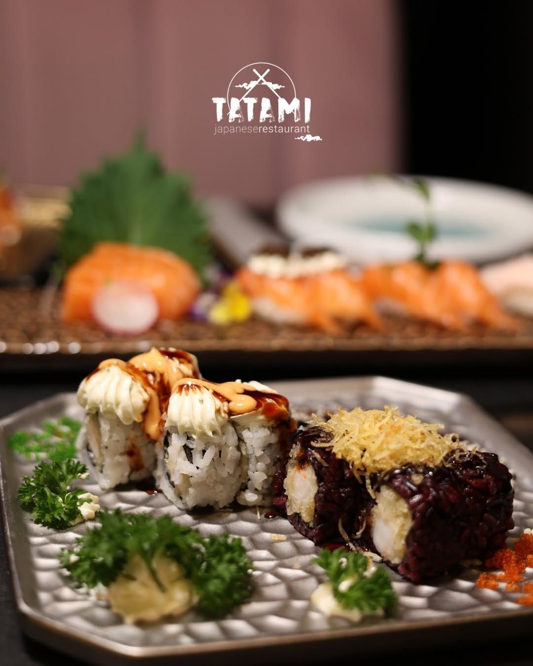 Assortimento di sushi su un piatto decorativo, con vassoi di sushi sfocati e il logo di un ristorante sullo sfondo