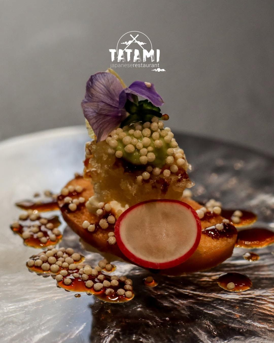 Antipasto gourmet impiattato con guarnizione viola e fettina di ravanello su un piatto di ceramica scura