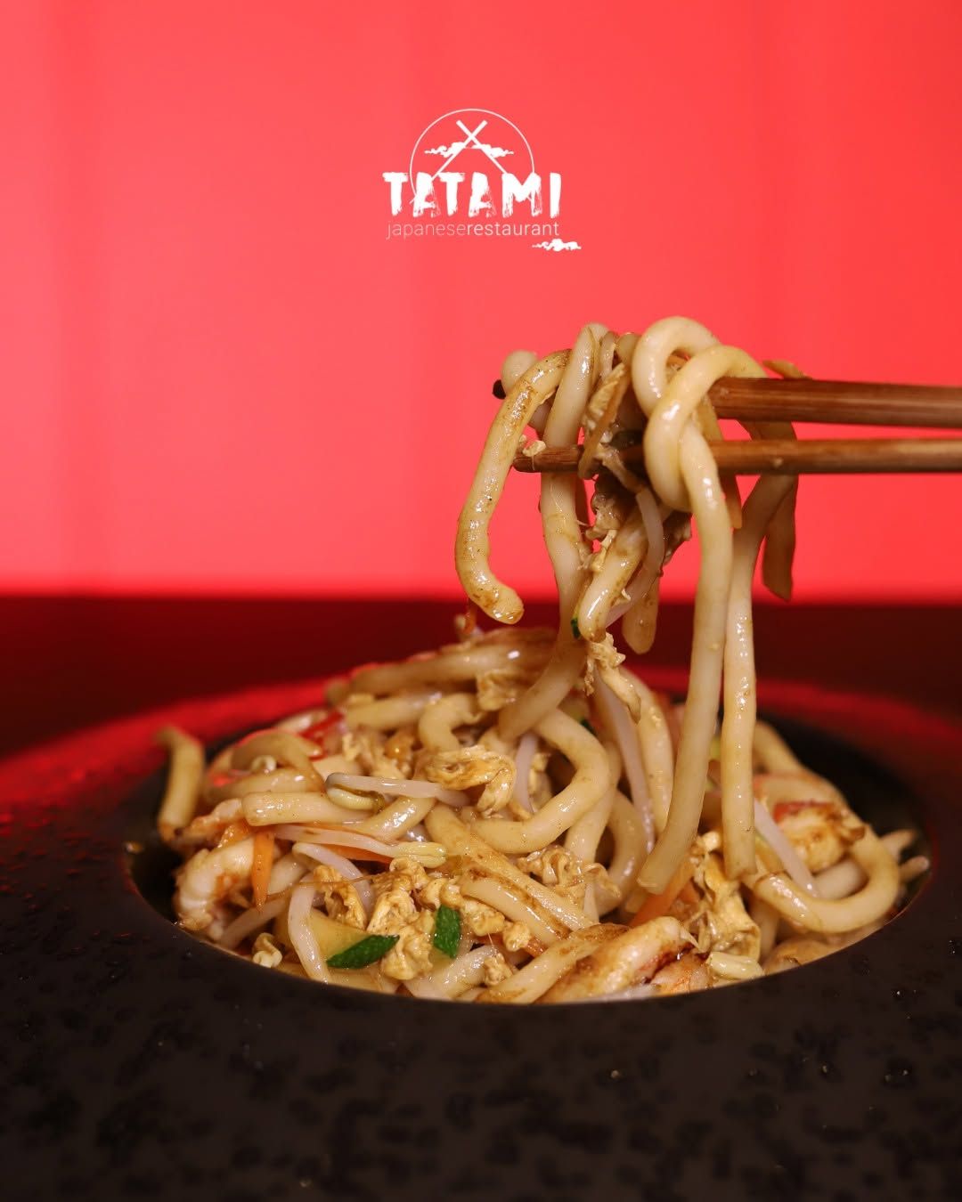 Bacchette che sollevano noodles da una ciotola nera su uno sfondo rosso