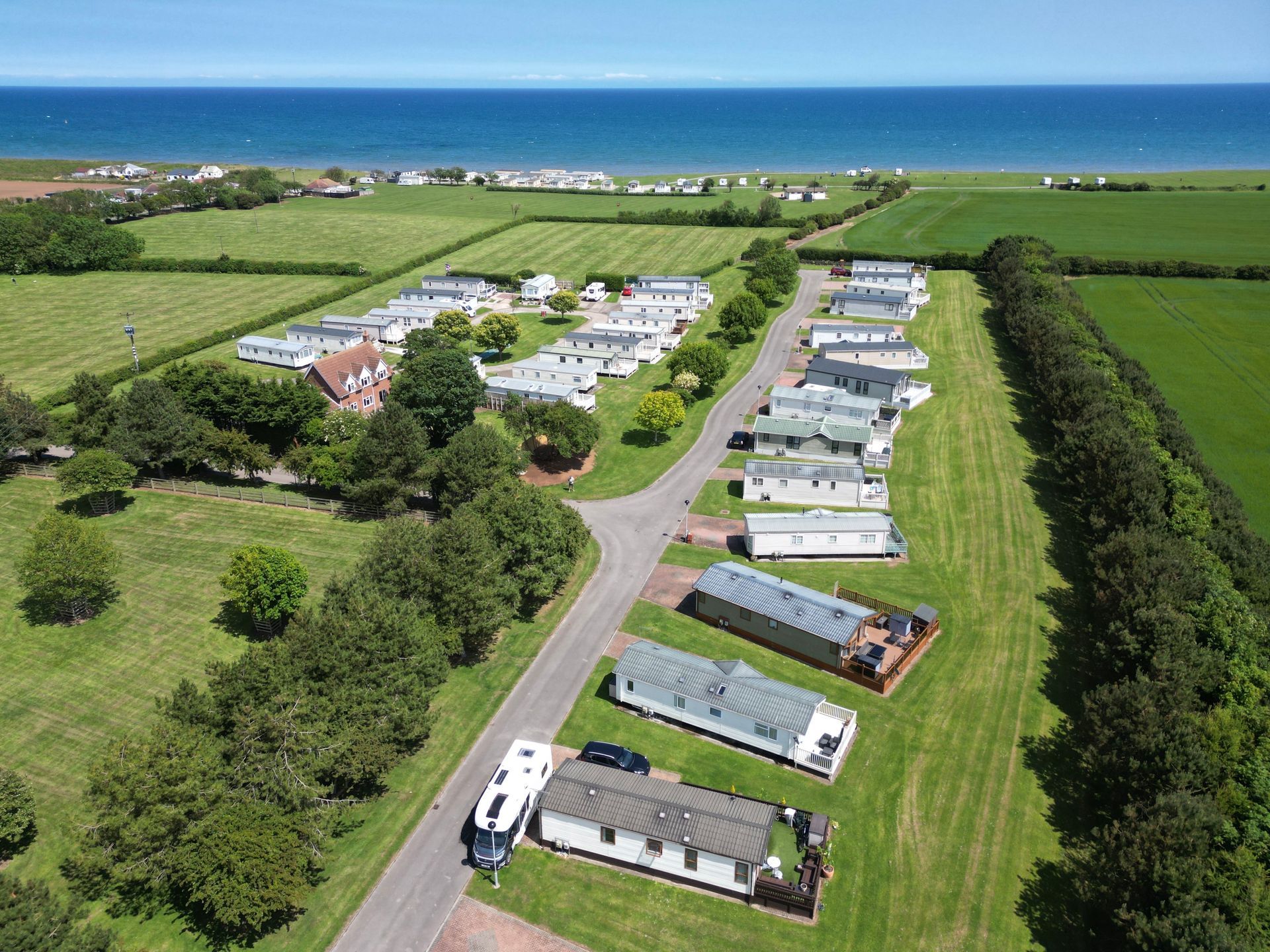 Aerial view: caravan park near the coast. Rows of caravans, green fields, and blue ocean visible.