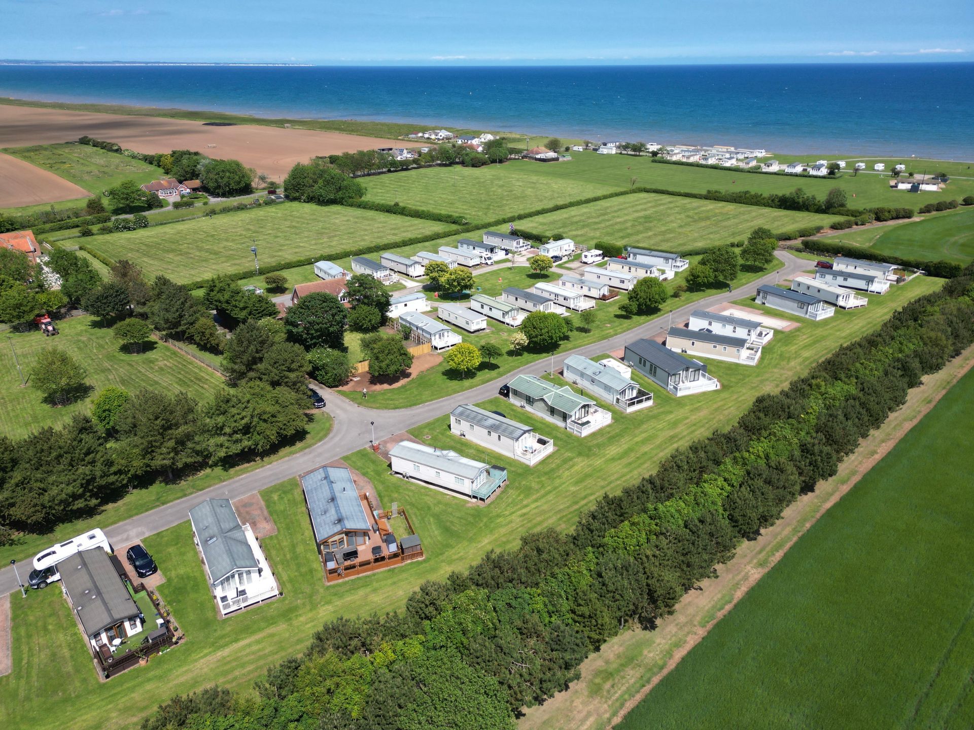 Aerial view of a caravan park near the sea, featuring rows of caravans, green fields, and blue water.