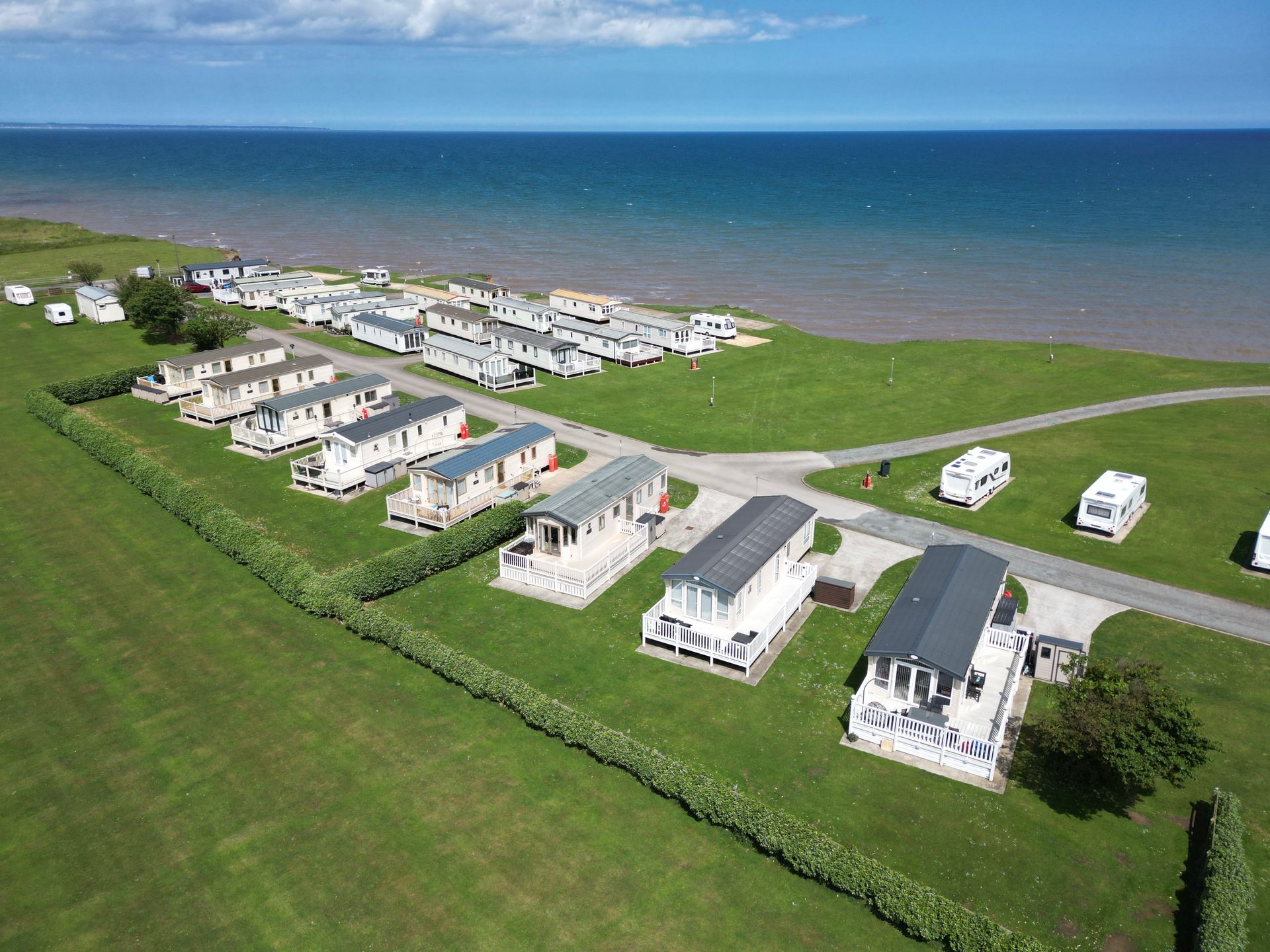 Aerial view of caravan park on a grassy shore, overlooking the blue sea under a sunny sky.