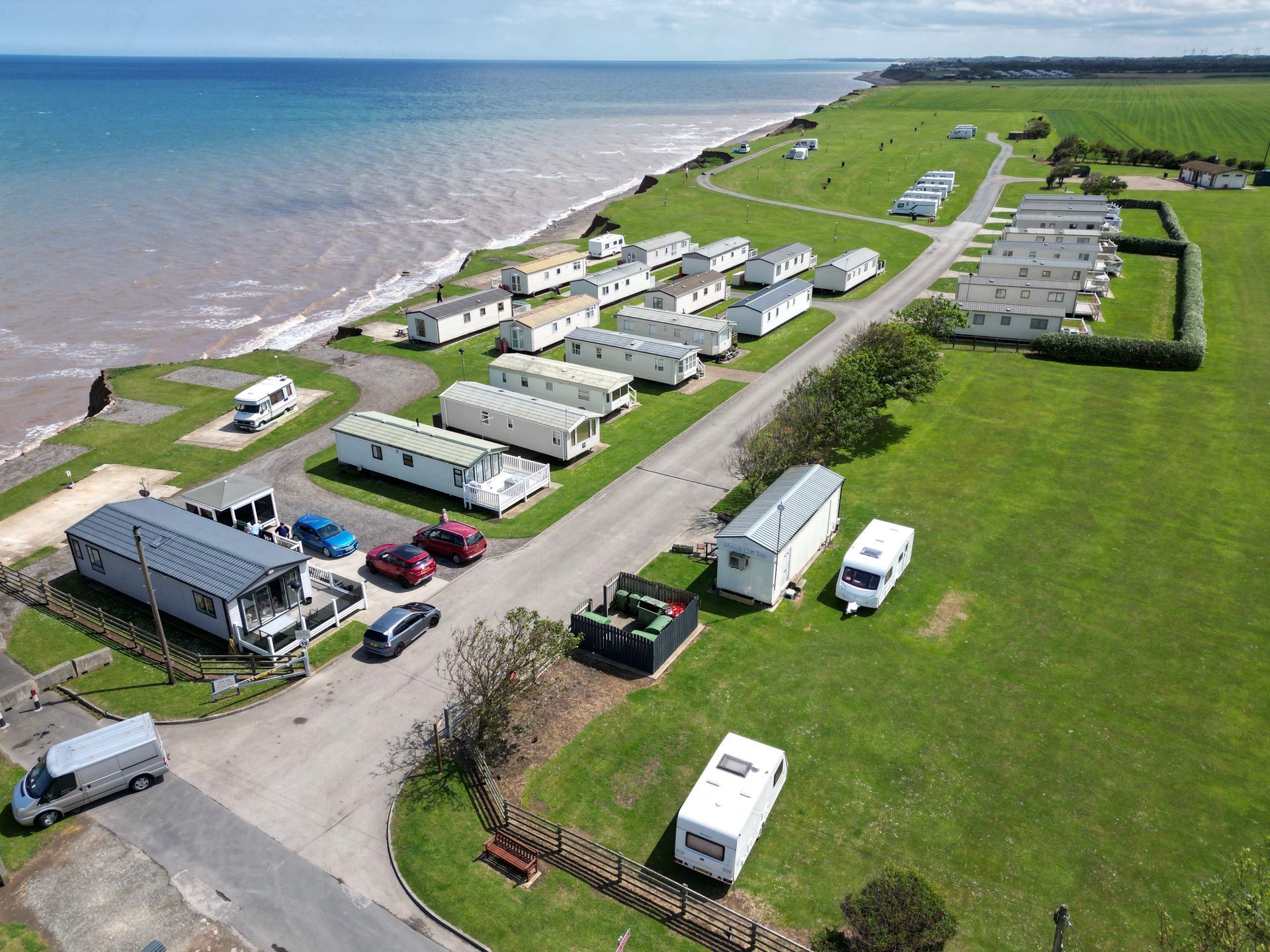 Coastal caravan park with rows of white trailers on a grassy cliff overlooking the sea.